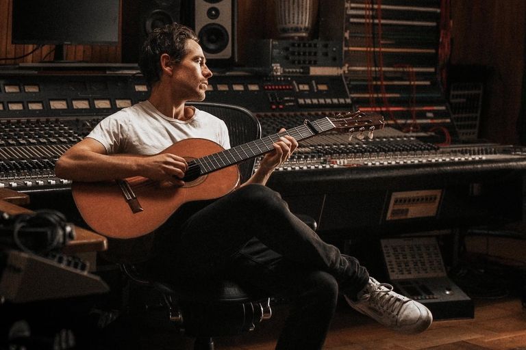 Singer-songwriter Mark Wilkinson playing acoustic guitar inside a recording studio sitting in front of a vintage mixing console.